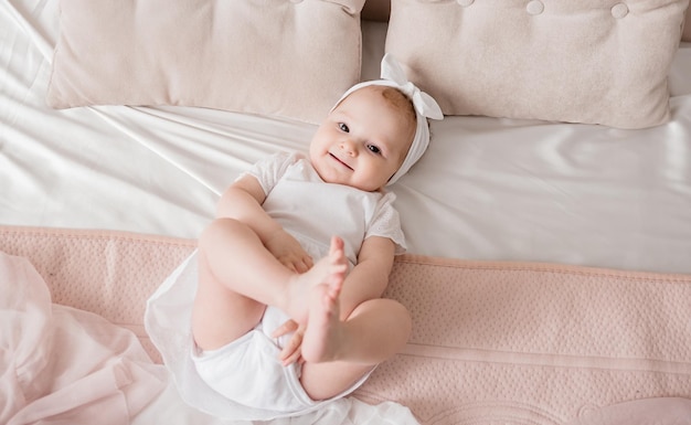 Foto uma menina caucasiana em uma faixa de cabeça e uma roupa branca está deitada na cama no quarto