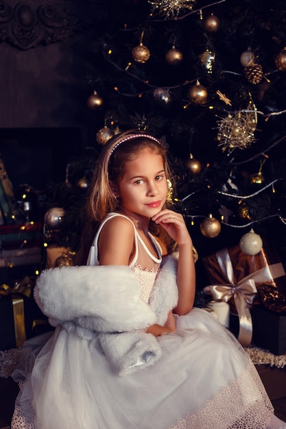 Uma menina com cabelo castanho em um fundo escuro com vestido bonito. Ouro e preto. Árvore de Natal e decorações de ano novo