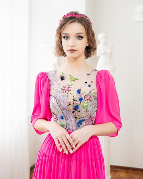 Uma menina com cabelo curto e um vestido rosa com uma coroa de flores na cabeça