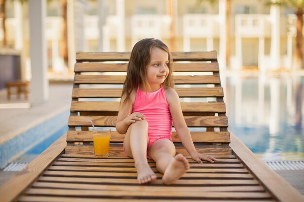 Uma menina com cabelo loiro colocando as mãos atrás da cabeça relaxando banhos de sol em um maiô rosa