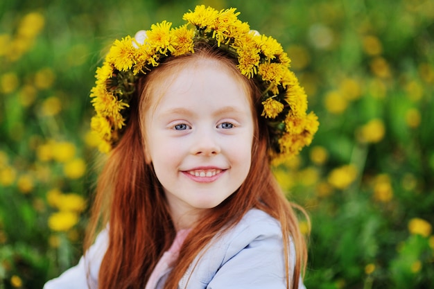 Uma menina com cabelo vermelho sorri contra um campo dos dentes-de-leão e da grama verde.