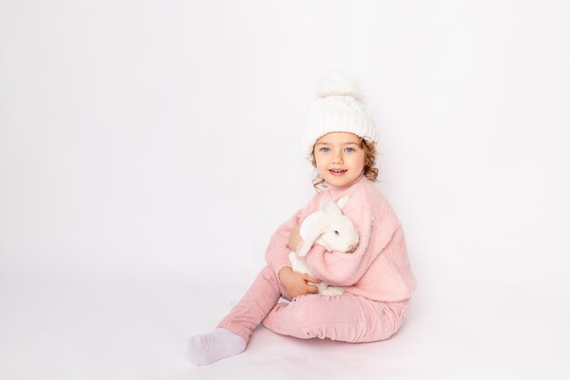 Uma menina com roupas de inverno segura um coelho em um fundo branco.