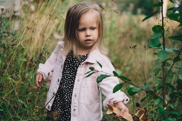 Uma menina com um avião de madeira está em uma clareira e olha pensativo sinceramente não emoções infantis feliz infância jogos ao ar livre