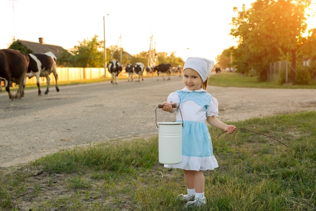 Uma menina com um balde nas mãos encontra um rebanho de vacas voltando de um pasto na aldeia