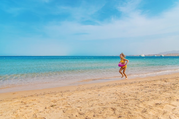 Uma menina com um biquíni amarelo e um anel inflável rosa corre pela praia