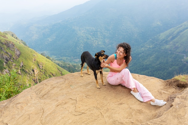 Uma menina com um cachorro, apreciando a paisagem montanhosa à beira de um precipício