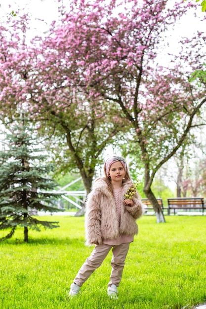 uma menina com um casaco de pele clara caminha entre árvores florescentes