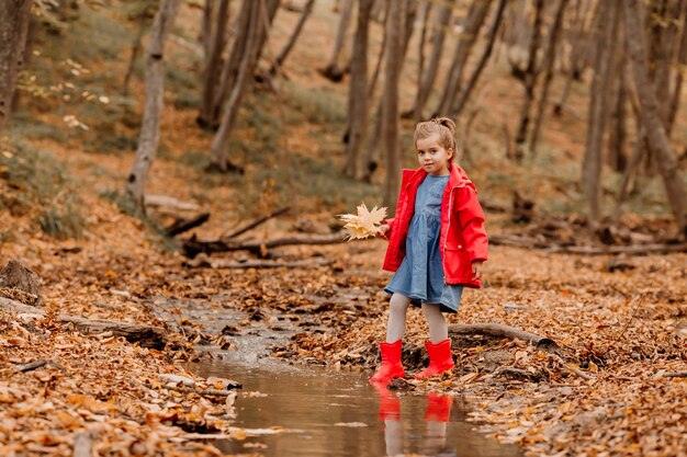 Uma menina com um casaco e botas de borracha vermelhas, caminhando na floresta de outono. Foto de alta qualidade