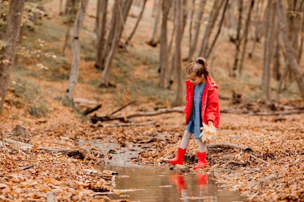 Uma menina com um casaco e botas de borracha vermelhas, caminhando na floresta de outono. Foto de alta qualidade