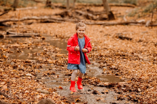 Uma menina com um casaco e botas de borracha vermelhas, caminhando na floresta de outono. Foto de alta qualidade