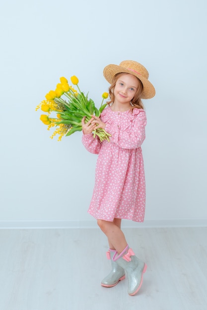 Uma menina com um chapéu de palha segura um buquê de tulipas amarelas isoladas em um fundo branco