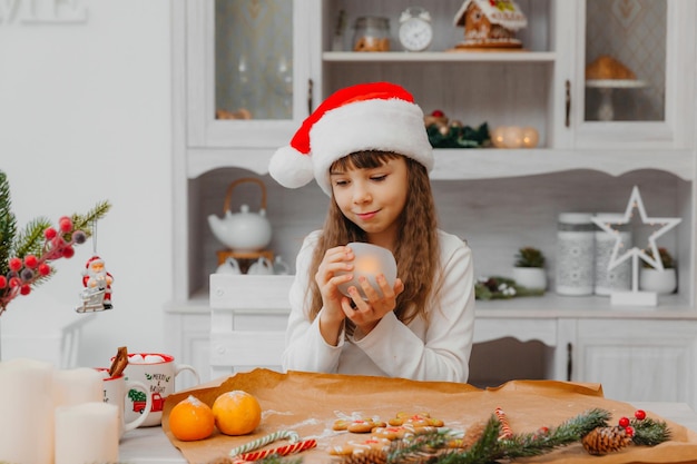 Uma menina com um chapéu de Papai Noel se senta à mesa da cozinha.