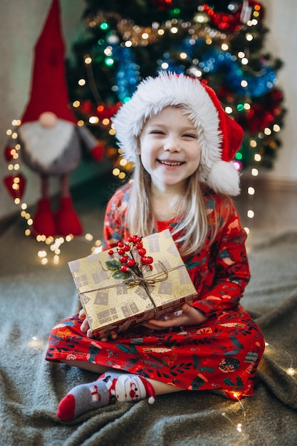 Uma menina com um chapéu vermelho de Papai Noel separa os presentes no contexto de uma árvore de Natal