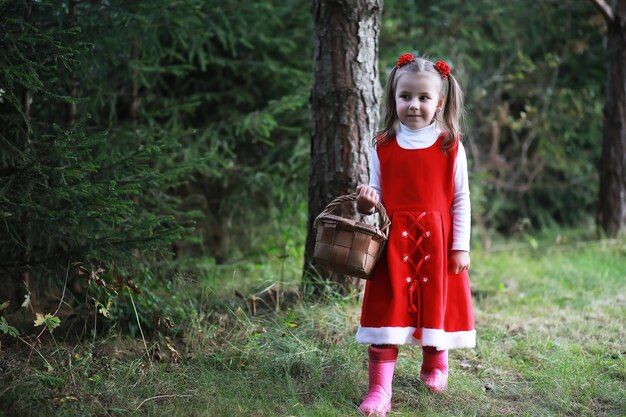 Uma menina com um chapéu vermelho e vestidos está caminhando no parque. Cosplay para o herói dos contos de fadas "Chapeuzinho Vermelho"