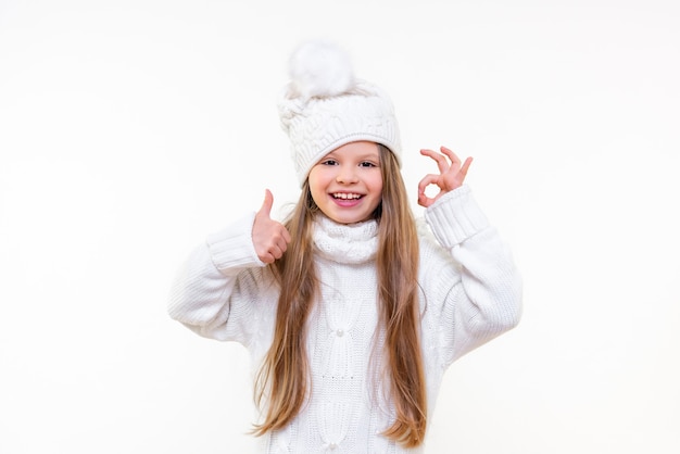 Uma menina com um suéter branco quente e um chapéu de inverno em um fundo branco e isolado.