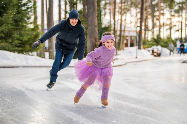 Uma menina com um suéter rosa e uma saia cheia cavalga em um dia ensolarado de inverno em uma pista de gelo ao ar livre no parque