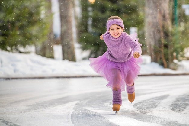 Uma menina com um suéter rosa e uma saia cheia cavalga em um dia ensolarado de inverno em uma pista de gelo ao ar livre no parque