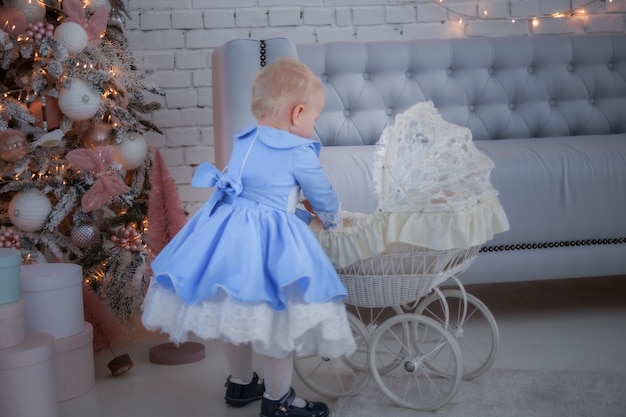 Uma menina com um vestido fofo e uma faixa na cabeça carrega um carrinho na sala festivamente com uma guirlanda