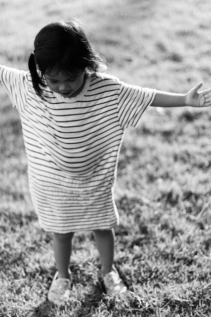Uma menina com um vestido listrado está em um campo gramado com os braços estendidos.