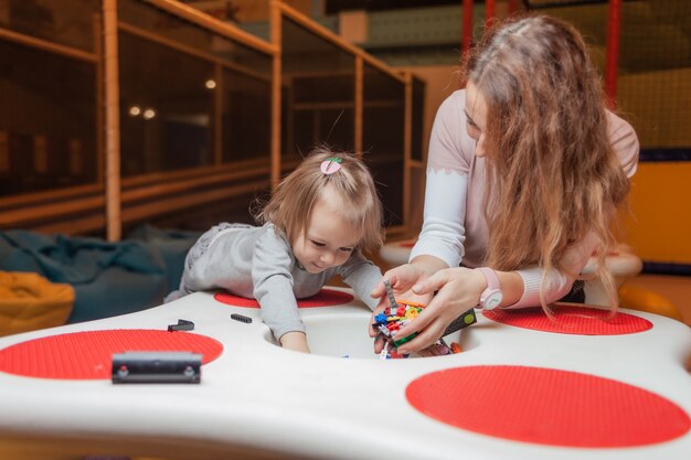 Uma menina com uma babá joga tijolos de brinquedo na mesa de um centro de entretenimento infantil