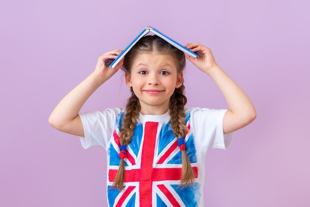 Uma menina com uma bandeira inglesa na camiseta segura um livro sobre a cabeça.