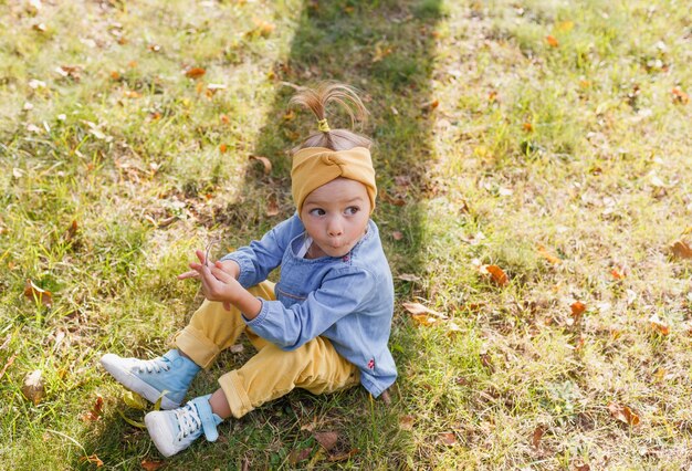 Foto uma menina com uma camisa azul e um rosto surpreso está sentada na grama do parque