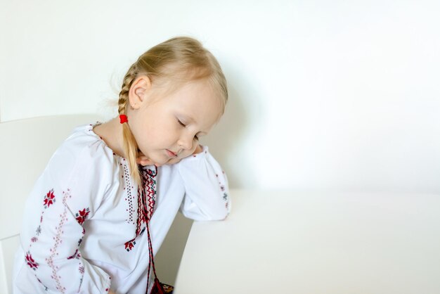 Uma menina com uma camisa bordada tradicional ucraniana adormeceu em uma aula em sua mesa branca