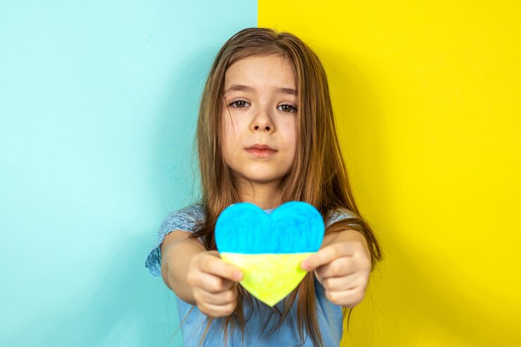 Foto uma menina com uma jaqueta azul mostra um coração pintado em tons amarelos e azuis