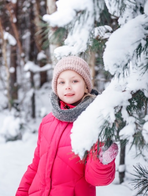 Uma menina com uma jaqueta brilhante joga na floresta de inverno nevado.