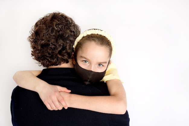 Uma menina com uma máscara antibacteriana preta e uma camiseta amarela nos braços do pai. A filha abraça o pai com força. Conceito de família, amor e cuidado.
