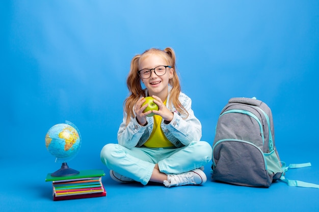 Uma menina com uma mochila e livros está sentada sobre um fundo azul