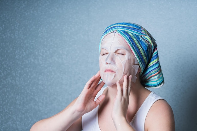 Foto uma menina com uma toalha na cabeça faz um procedimento cosmético em casa usando uma máscara facial para cuidar da pele