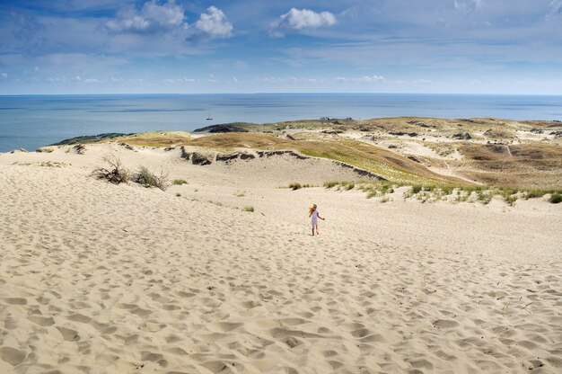 Uma menina corre pelas dunas de areia até o Mar Báltico em tempo ensolarado. Lituânia.