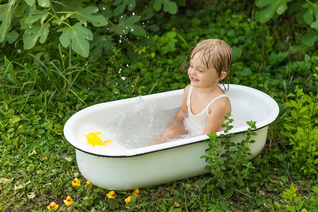 Uma menina criança em um banho retrô banha-se na natureza e ri.