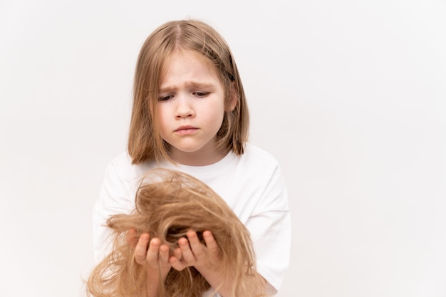 Foto uma menina criança triste segura nas mãos cortadas o cabelo após o corte em um fundo branco. significa cuidar do cabelo das crianças. salão de beleza para crianças.