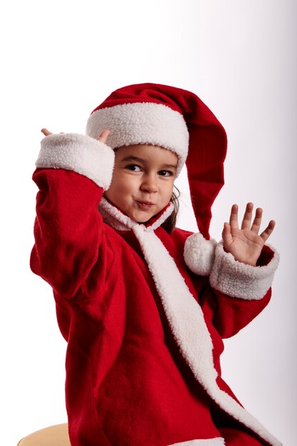 Uma menina cumprimenta a câmera vestida de Papai Noel.