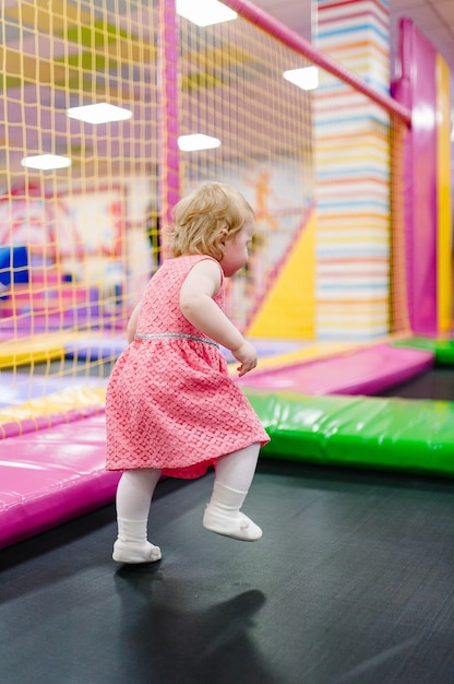 Uma menina de 1-2 anos brincando e pulando em um trampolim na sala de jogos infantil para seu aniversário. Centro de entretenimento.