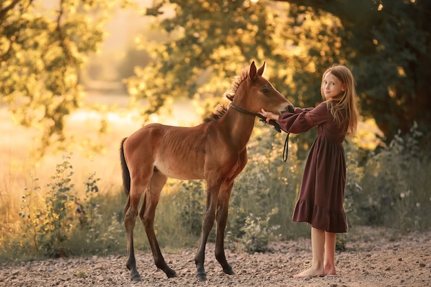 Uma menina de 12 anos anda descalça em um campo com um cavalo pequeno