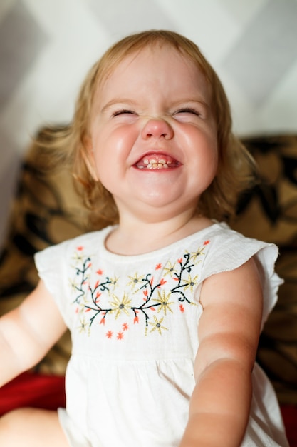 Uma menina de 2 anos está sentada na cama e sorrindo. A criança se alegra e se vira. Criança Feliz