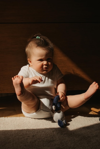 Uma menina de 7 meses está sentada no tapete vestida de bodysuit em casa