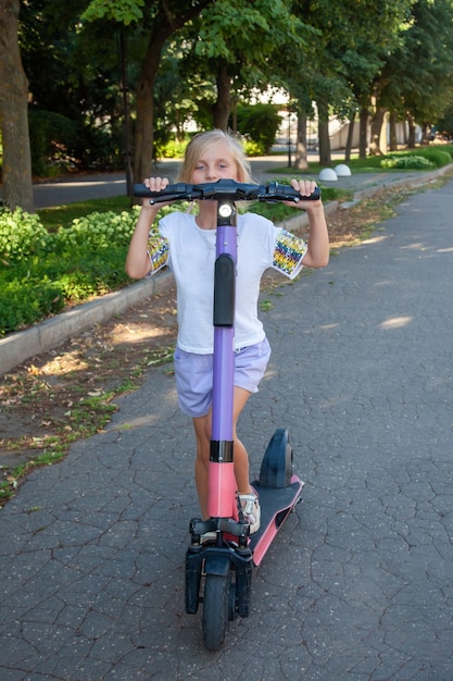 Uma menina de 8 anos anda de scooter elétrica alugada no parque. compartilhamento de scooter de chute