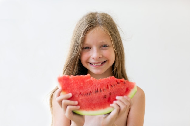 uma menina de 9 anos com olhos azuis e cabelos longos com um pedaço de melancia vermelha madura e um sorriso