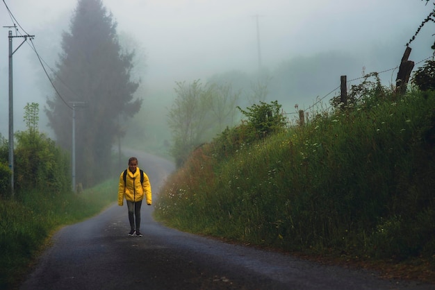 Uma menina de 9 anos com uma mochila vai para a escola ao longo de uma estrada rural de manhã sozinha na primavera