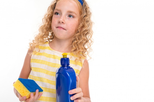 Uma menina de cabelos vermelhos em um terno de verão listrado branco e amarelo, com um curativo azul na cabeça com uma esponja e detergente