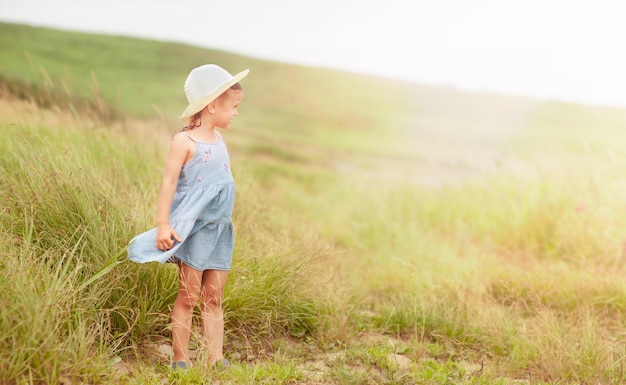 uma menina de chapéu está de pé no meio do campo e olhando para a luz do sol