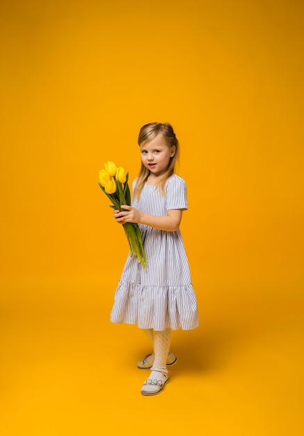 Uma menina de corpo inteiro com um buquê de tulipas amarelas