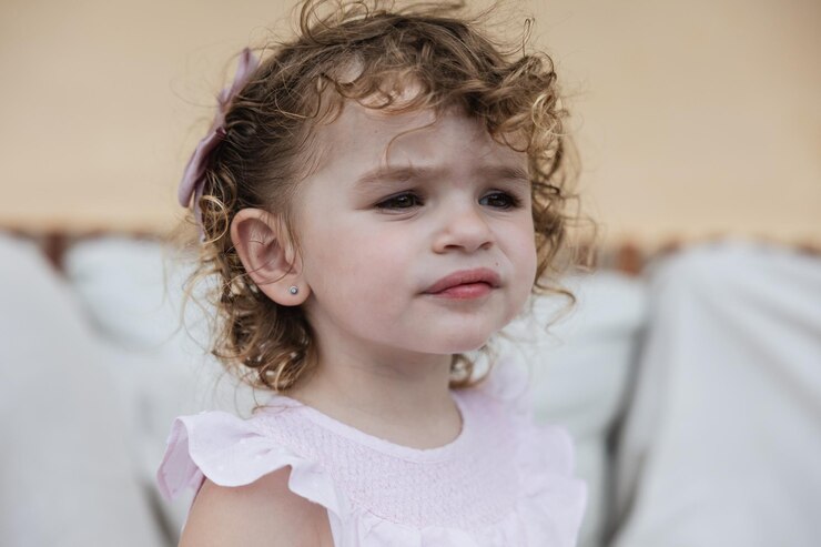 Foto uma menina de dois anos com um olhar pensativo e cabelos encaracolados.