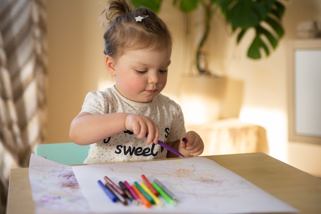 Foto uma menina de dois anos está sentada a uma mesa e desenhando a lápis