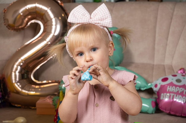 Foto uma menina de dois anos sopra um cachimbo em seu aniversário