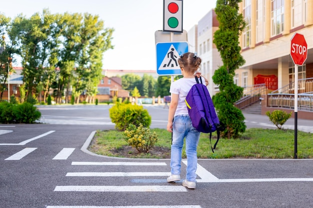 uma menina de escola atravessa a estrada em uma zebra perto do sinal de estrada pedestre atravessando indo para a escola com uma mochila o conceito de regras de trânsito